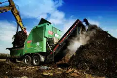A digger turning an industrial compost heap.